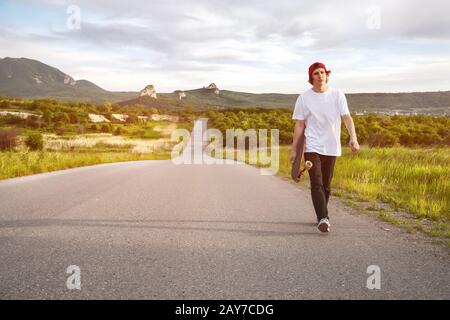 Un uomo in un berretto e con una lunga tavola nelle sue mani sta camminando su una strada di campagna Foto Stock