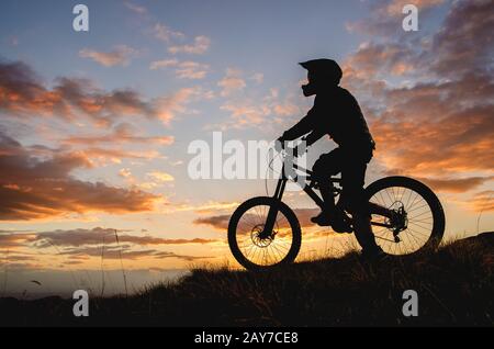 Silhouette di un ciclista su una bicicletta sportiva sullo sfondo del tramonto sole in montagna Foto Stock