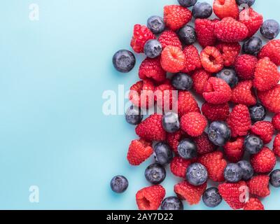 Lampone e mirtillo su sfondo blu con spazio di copia Foto Stock