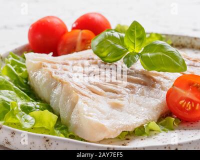 Chiudere il codfish alla griglia con basilico e pomodori ciliegini Foto Stock