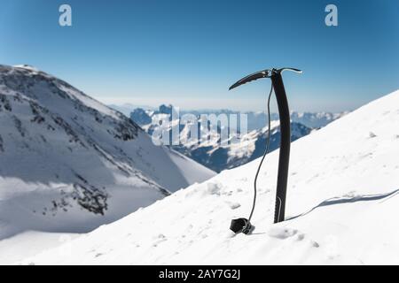 Ice AX nella neve sullo sfondo di rocce innevate. Foto Stock