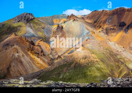 Viaggio in Islanda nel mese di luglio. Montagne multicolore dalla riolite minerale sono illuminate dal sole. Tundra vulcanica estiva Foto Stock
