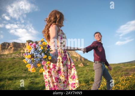 Giovane coppia sposata. Il ragazzo conduce una ragazza curly con un bouquet di fiori. Foto Stock