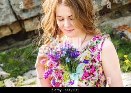 Una ragazza in un abito colorato tiene un bouquet di fiori selvatici Foto Stock