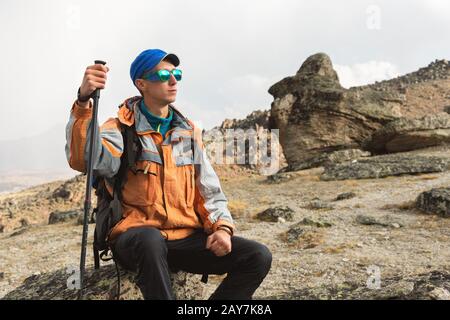 Un turista solitario con uno zaino e occhiali da sole è seduto su una roccia Foto Stock