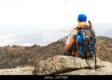 Un turista solitario con uno zaino e occhiali da sole è seduto su una roccia Foto Stock