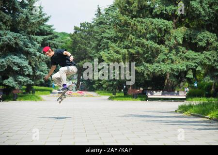 Skater-teenager dai capelli lunghi in una T-shirt e un cappello da sneaker salta un vicolo contro un cielo tempestoso Foto Stock