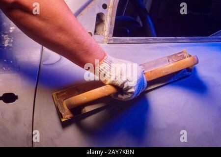 Riparazione carrozzeria auto, rettifica parti con utensile manuale in condizioni di garage, illuminazione blu astratta. Foto Stock