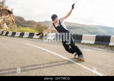 Longboarder su longboard in tuta casco e guanti esegue uno stand-up slide a velocità mentre su una strada di montagna serpentina in Foto Stock