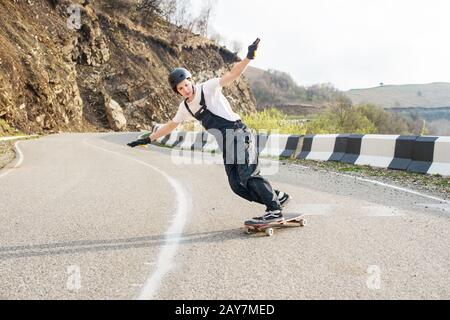 Longboarder su longboard in tuta casco e guanti esegue uno stand-up slide a velocità mentre su una strada di montagna serpentina in Foto Stock