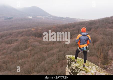 Hippster - uno scalatore in una giacca in giù e un supporto a maglia del cappuccio e si appoggia sulla cima di una roccia Foto Stock