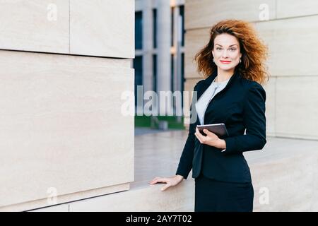 Donna dall'aspetto piacevole, vestita formalmente, con un tablet digitale che è necessario per il suo lavoro. Bella donna con capelli maledini, havin Foto Stock