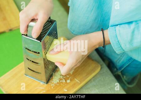 Primo piano delle mani di una donna strofinare il parmigiano su una grattugia metallica. Foto Stock