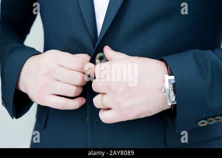 Una verruca newlywed con una barba in un vestito fissa il tasto della sua giacca. Super primo piano. Foto Stock