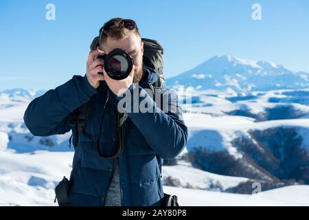 Ritratto di un hippster barbuto, fotografo con uno zaino e occhiali da sole scatta foto della sua DSLR Foto Stock