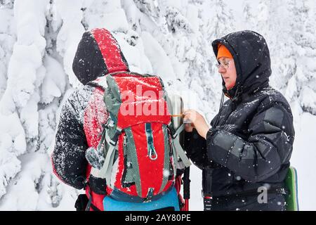 due escursionisti in una foresta invernale innevata vogliono riscaldarsi, una donna prende un thermos dal suo zaino amico Foto Stock