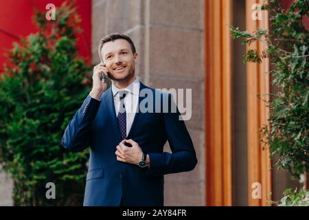 Ritratto di bel successo colloqui d'affari soddisfatti sul telefono cellulare, discute le transazioni bancarie, vestito in abito aziendale, ha exp positivo Foto Stock