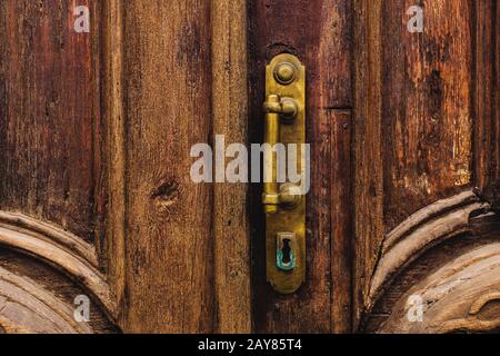 Sfondo vintage. Vecchia maniglia in ottone con elementi di una porta in legno intagliato decorata con massiccio tessuto in legno simulante Foto Stock