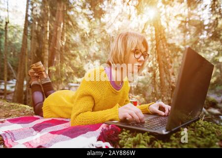 Immagine tonata di una ragazza freelancer ritratto in un maglione giallo e occhiali che guarda con attenzione lo schermo del laptop in Europa Foto Stock