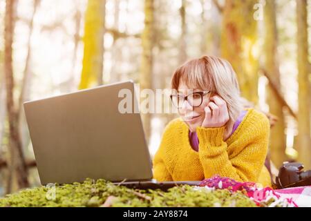 Immagine ravvicinata Di una ragazza freelancer ritratto in un maglione giallo e occhiali che guardano con attenzione lo schermo del laptop dentro Foto Stock