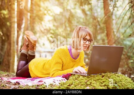 Immagine tonata di una ragazza freelancer ritratto in un maglione giallo e occhiali che guarda con attenzione lo schermo del laptop in Europa Foto Stock