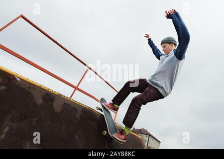 Un teenager skateboarder in un cappello fa un trucco Rocks su una rampa in un parco skate contro un cielo nuvoloso e zona notte. Il concep Foto Stock