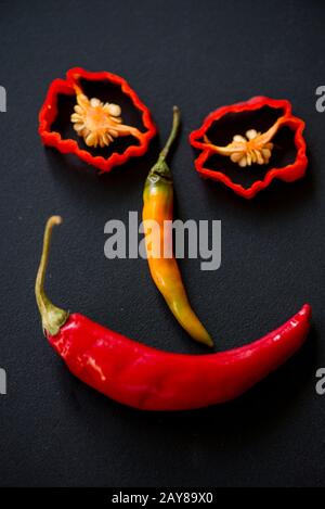 Sorridente divertente viso fatto con peperoncino piccante su ardesia nera Foto Stock