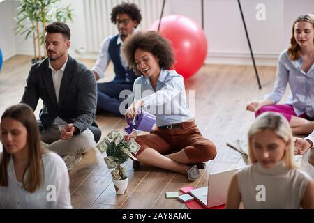 gruppo di colleghi di lavoro che meditano sul lavoro, seduti sul pavimento, una donna che fa la visualizzazione del reddito di denaro aumentare. moderno, business, medi Foto Stock