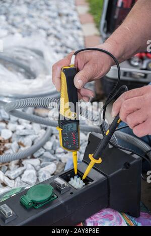 L'elettricista controlla la tensione della presa con il tester di tensione Foto Stock