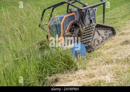 Il robot con falciatrice anteriore taglia l'erba in terrapieno - primo piano Foto Stock