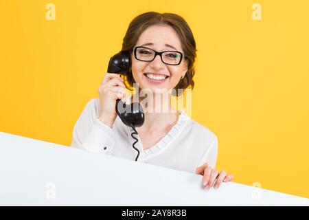 Ritratto di sicuro bello eccitato sorridente felice giovane donna di affari con telefono che mostra tabellone in bianco sul retro giallo Foto Stock