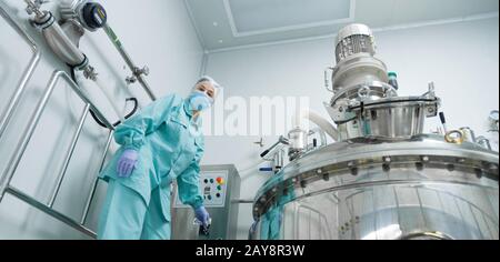 Fabbrica farmaceutica donna lavoratrice in abbigliamento protettivo di funzionamento della linea di produzione in ambiente sterile Foto Stock