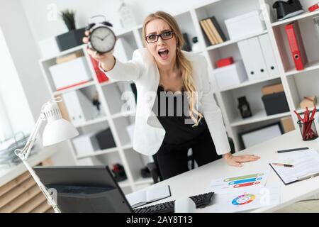 Una giovane ragazza si erge nei pressi di un tavolo in ufficio e detiene una sveglia. Foto Stock