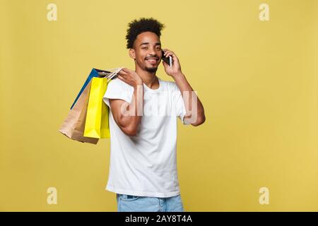 Giovane con le borse della spesa a parlare su smart phone isolato su sfondo giallo Foto Stock