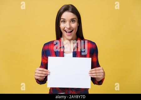 Stupore o sorpresa femmina con vuoto pannello bianco, isolato su sfondo giallo. Foto Stock