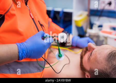 Medico di emergenza le mani, fissaggio elettrodi ECG sul torace del paziente in ambulanza Foto Stock