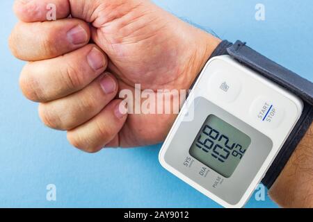 Mano maschile che indossa il monitor della pressione sanguigna da polso bianco e grigio su sfondo blu Foto Stock