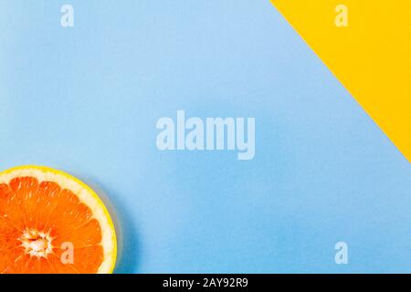 Primo piano su una singola fetta di pompelmo su sfondo blu e diagonale giallo Foto Stock