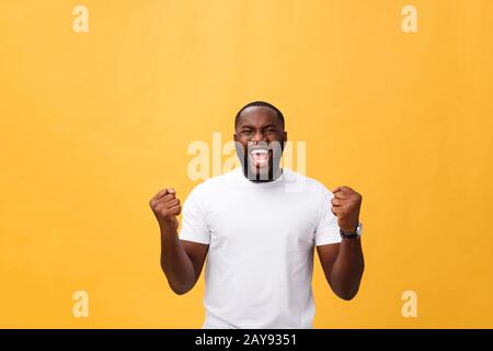 Bel giovane dipendente afro-americano si sente eccitato, gesturando attivamente, mantenendo i pugni stretti, esclamato con gioia Foto Stock