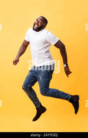 Lunghezza completa di bel giovane uomo nero jumping contro sfondo giallo. Foto Stock