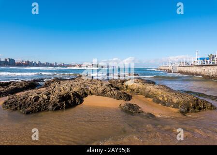 Gijon, Spagna - 19 Novembre 2018: Spiaggia di San Lorenzo e il turista a camminare su una passeggiata in una giornata di sole Foto Stock