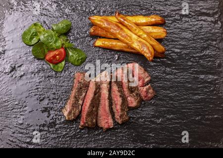 Fette di bistecca con patatine fritte su ardesia Foto Stock