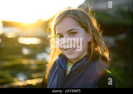 Ritratto retroilluminato al tramonto di un ragazzo dai capelli lunghi sorridente alla fotocamera Foto Stock