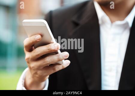 Close-up Smart Business uomo che indossa Moderna tuta nera e una camicia bianca e gli sms sul cellulare smart phone. Foto Stock
