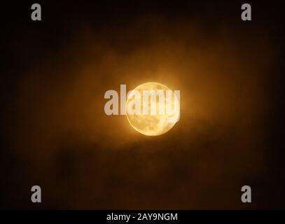 la luna super piena rossa si illuminava contro le nuvole in un cielo scuro Foto Stock