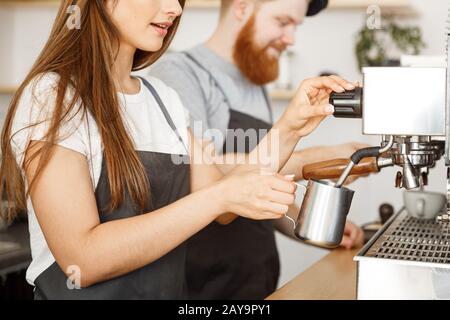 Coffee Business Concept - ritratto di signora barista in grembiule preparare e montare il latte per l'ordine del caffè con il suo partner mentre Foto Stock