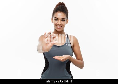 Concetto di salute e di idoneità - ritratto di closeup della bella African American che prende una pillola di olio di fegato Del Merluzzo. Isolato su bianco s. Foto Stock