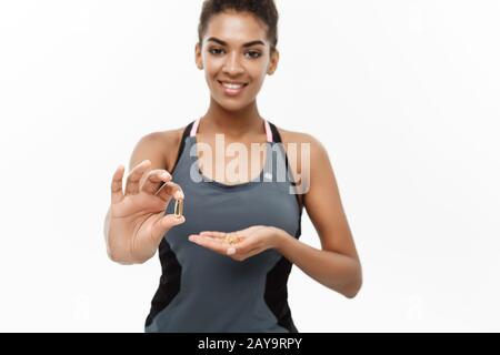 Concetto di salute e di idoneità - ritratto di closeup della bella African American che prende una pillola di olio di fegato Del Merluzzo. Isolato su bianco s. Foto Stock