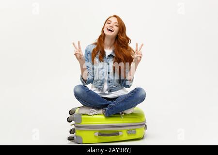 Concetto di viaggio: giovani caucasici sorridente donna posa sulla valigia che mostra due dita. Isolato su sfondo bianco. Foto Stock