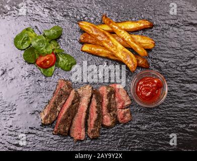 Fette di bistecca con patatine fritte su ardesia Foto Stock